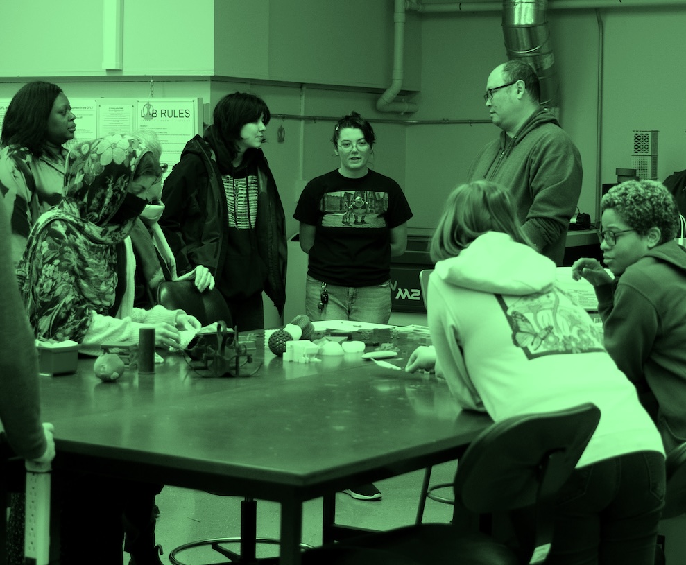 students and faculty stand around a table looking at 3D work